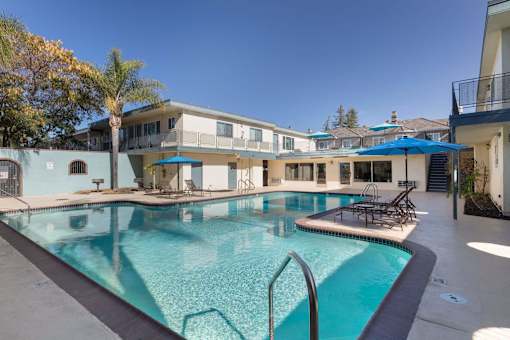 A swimming pool in front of a building with a blue umbrella.