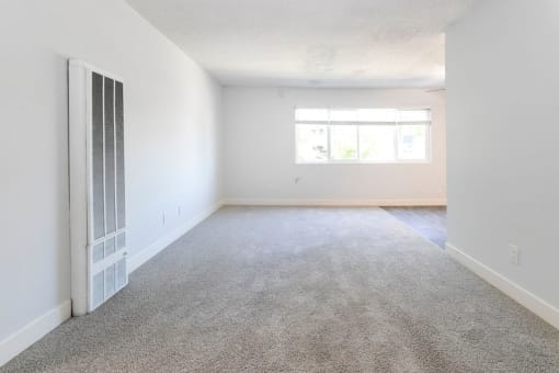 an empty living room with white walls and carpet and a window