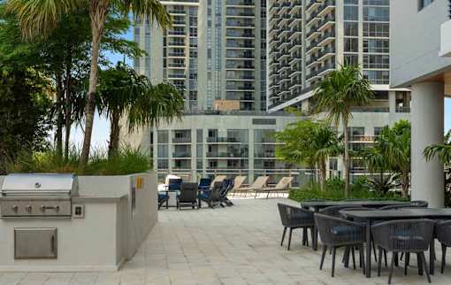 A patio with a grill and chairs overlooks a cityscape.