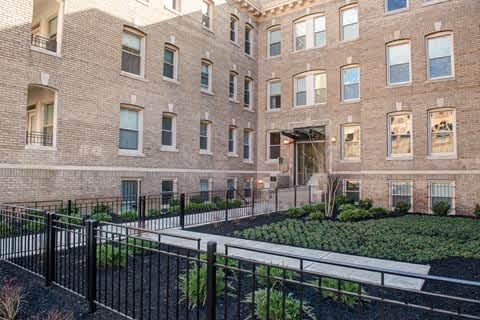 A large brick building with a black fence and a garden in front.