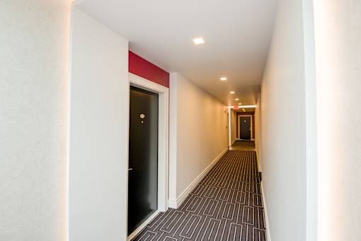 A long hallway with a black door on the left and a red stripe on the wall.