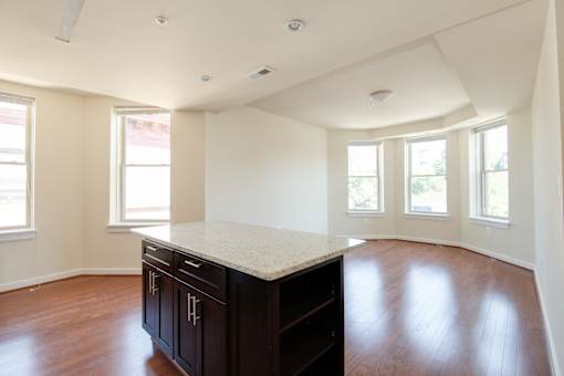 A large empty room with a kitchen island and wooden floors.