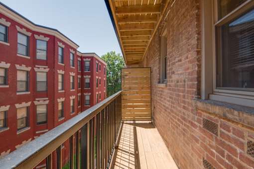 A balcony with a wooden railing and a brick building in the background.