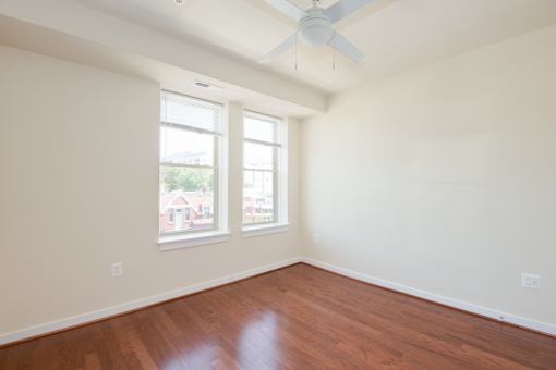 Empty room with a ceiling fan and two windows.