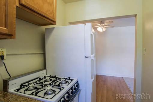 A white refrigerator with a black handle is in a kitchen with a stove and wooden cabinets.