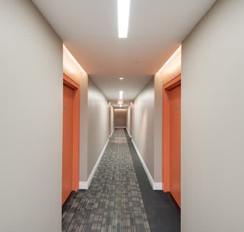 A long hallway with orange doors and a carpeted floor.