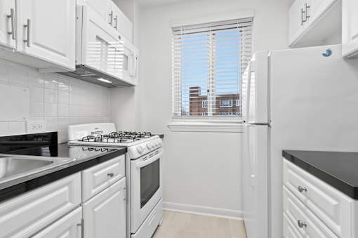 A white kitchen with black countertops and a window.