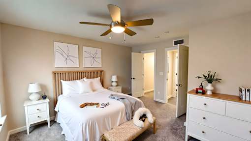 A bedroom with a large bed, a ceiling fan, and a small dog.