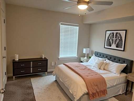 A bedroom with a bed, a dresser, and a ceiling fan.
