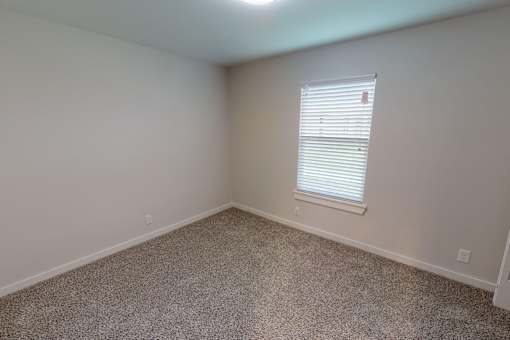 A room with a carpeted floor and a window with blinds.