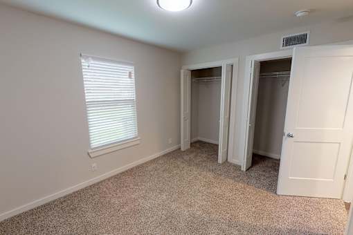 A room with a carpeted floor, a window with blinds, and a white door.