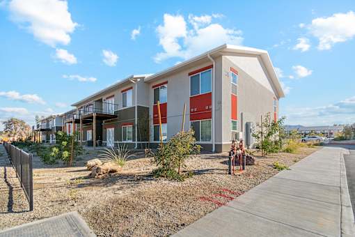 A modern building with a red door and windows is surrounded by a gravel area and a concrete walkway.