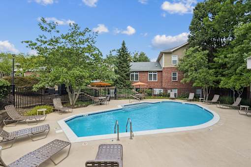 A pool surrounded by lounge chairs and trees.
