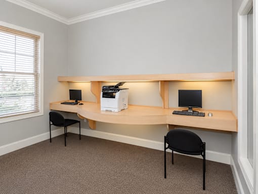 Two black chairs are placed in front of a desk with a computer and a printer.