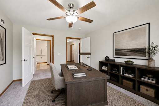 A room with a ceiling fan and a desk with a chair.