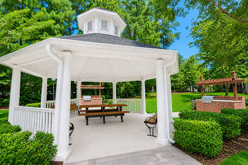 A white gazebo with a black roof and a white railing is surrounded by green bushes.