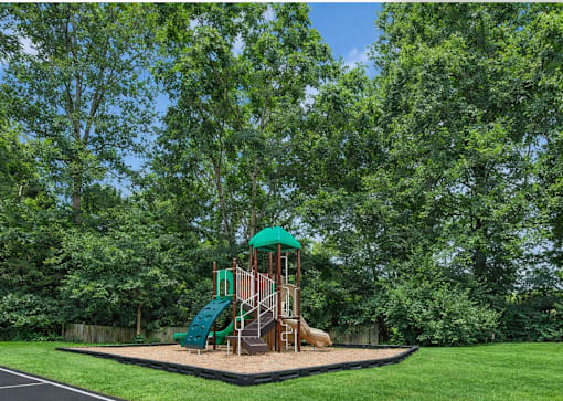 A playground with a green slide and a brown structure surrounded by trees.