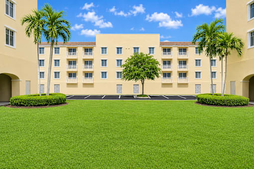 A large building with a green lawn in front and palm trees on the side.