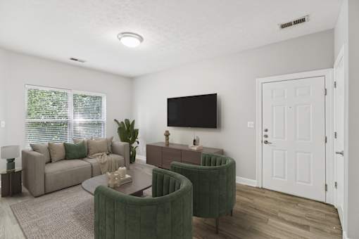 A living room with a grey couch, a green armchair, and a television mounted on the wall.