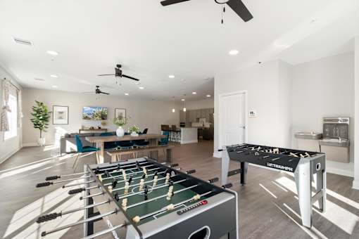 A foosball table is in the middle of a room with a ping pong table in the foreground.
