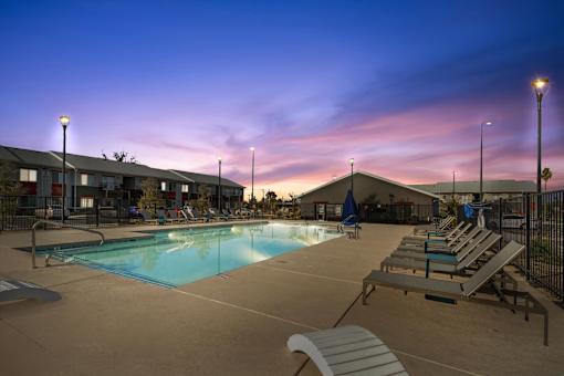 A pool area with sun loungers and a building in the background at dusk.