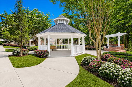 A gazebo is surrounded by a white picket fence and a variety of flowers.