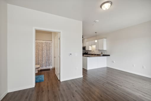 a spacious living room and kitchen with white walls and wood flooring