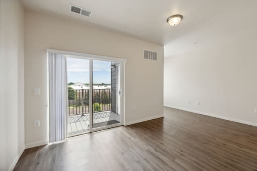 A bright living room with wood-style flooring, a sliding glass door leading to an outdoor space, and natural light coming in from outside.
