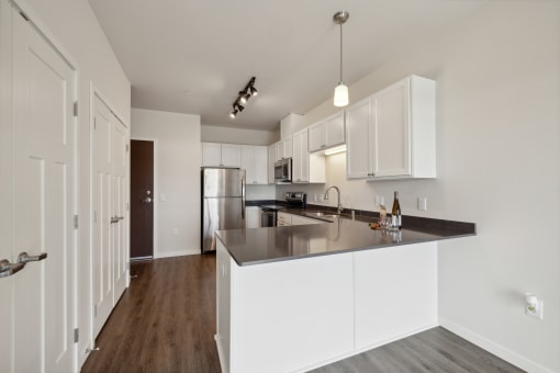 A spacious kitchen with modern white cabinetry, a large countertop, stainless steel appliances, and pendant lighting.