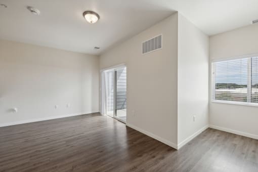 A spacious room with wood-style flooring, a sliding glass door leading to an outdoor area, and a ceiling light fixture. The walls are painted neutral tones.