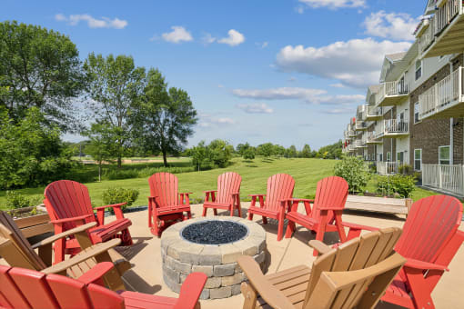 a patio with red chairs and a fire pit and an apartment building