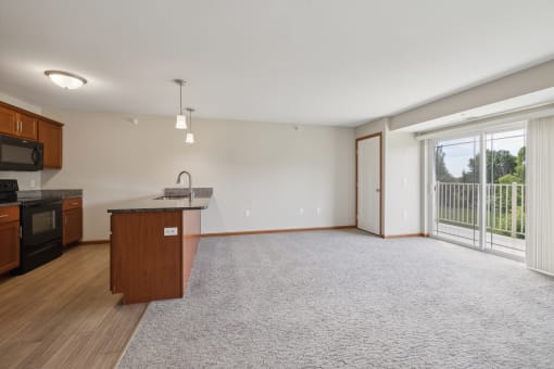 an empty living room with a kitchen and a large window