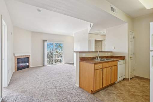 A spacious living room with a fireplace and a kitchen area with wooden cabinets and white appliances.