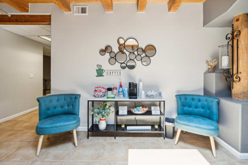 a living room with two blue chairs and a table and a wall with a shelf