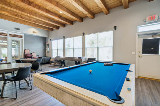 A pool table is in the middle of a room with a man sitting on a chair.