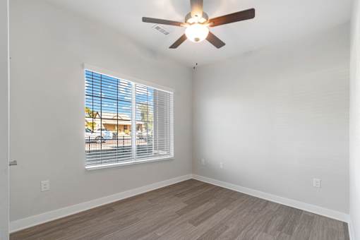 A room with a ceiling fan and a window with blinds.