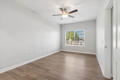 A room with a ceiling fan and a window showing trees outside.