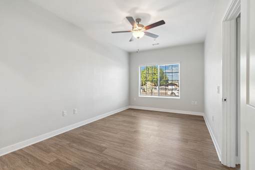 A room with a ceiling fan and a window showing trees outside.