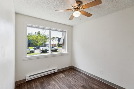 the living room of an apartment with a large window and a ceiling fan
