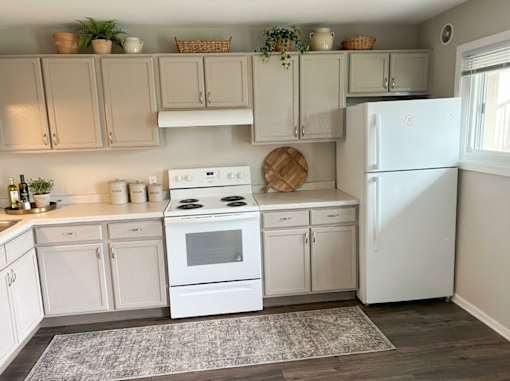 A white kitchen with a white fridge and white cabinets.