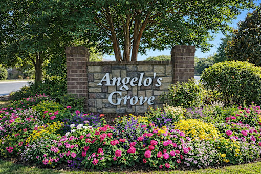 A sign that says "Angelo's Grove" in front of a flower bed.