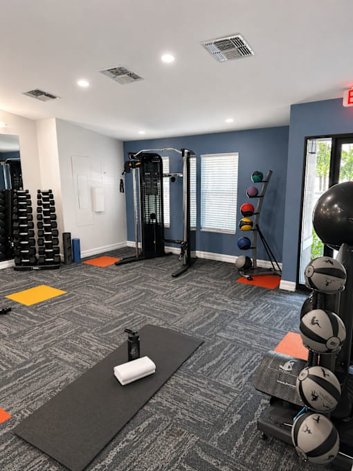 A gym with a variety of equipment including weights and a yoga mat.