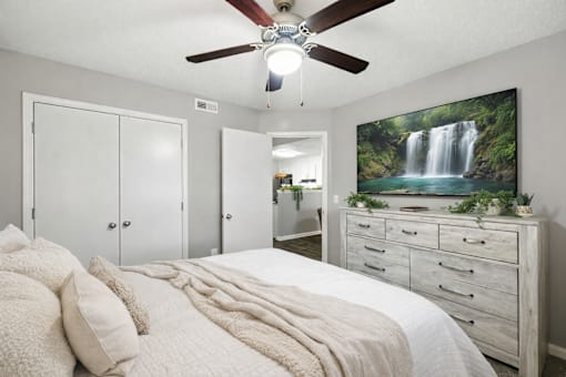 A bedroom with a large bed, a ceiling fan, and a waterfall mural on the wall.