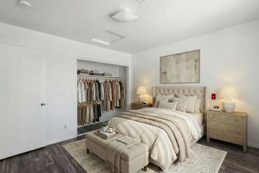 A bedroom with a large bed, a clothing rack, and a nightstand with lamps.