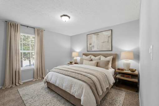 A bedroom with a large bed and a window with curtains.
