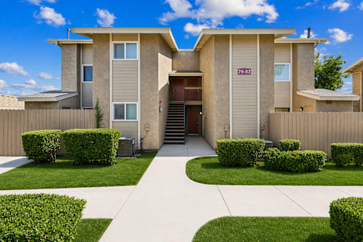 A beige two-story house with a driveway and green bushes.