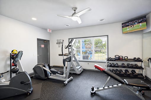 A gym with a row of treadmills, a stationary bike, a rowing machine, and a television showing a baseball game.