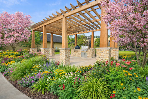 A wooden pergola stands over a garden with a stone wall and a pathway.