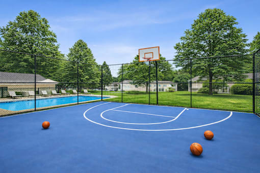 A basketball court with a blue surface and three basketballs on it.