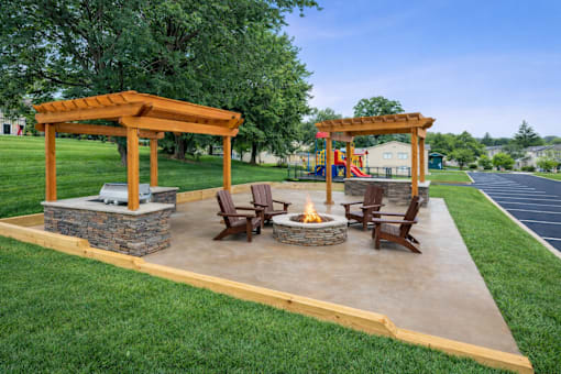 A patio with a fire pit and chairs under a wooden pergola.